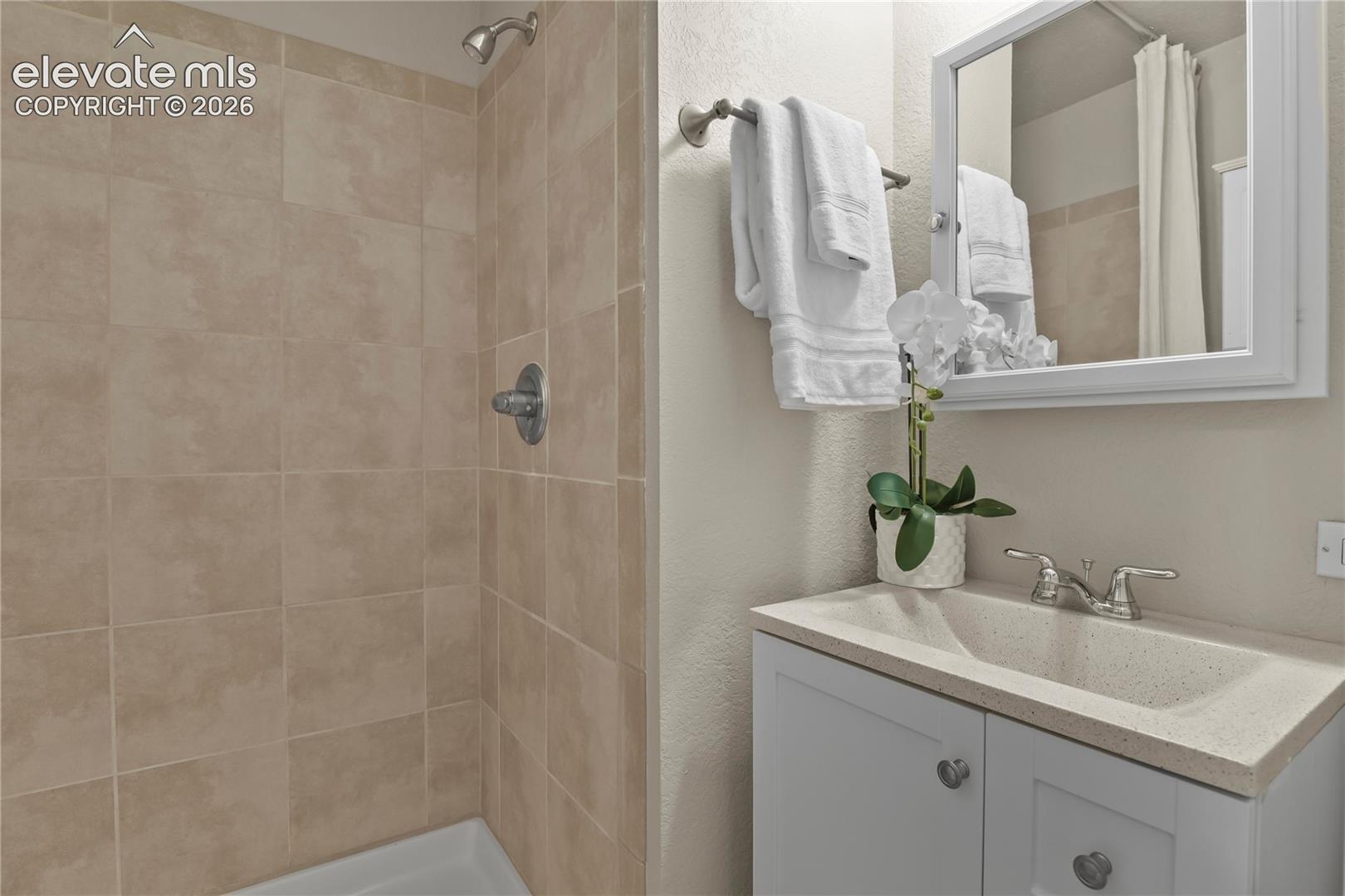 Bathroom featuring a shower stall with neutral tile surround, vanity with an integrated basin, and a wall-mounted medicine cabinet