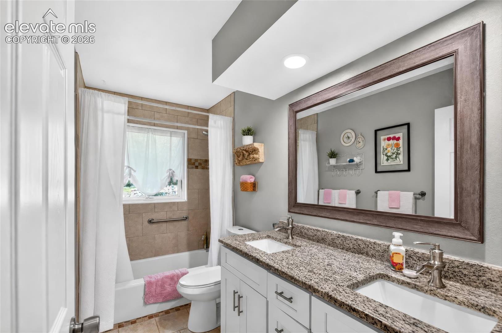 Bathroom featuring a dual vanity with granite countertops, undermount sinks, and a framed wall mirror
