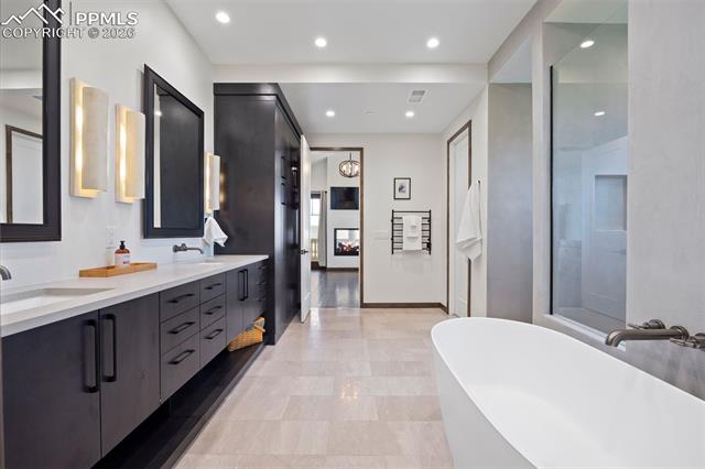 Spa-inspired primary bath with freestanding soaking tub, dual vanities, towel warmer, and walk-in shower.