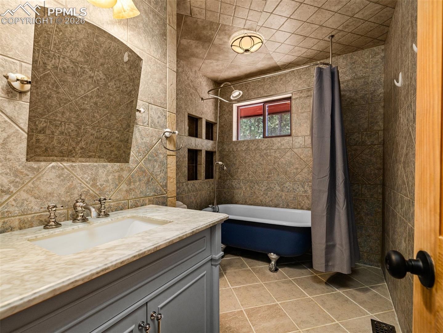 Full bathroom with vanity, tile walls, shower / bathtub combination with curtain, and light tile patterned flooring