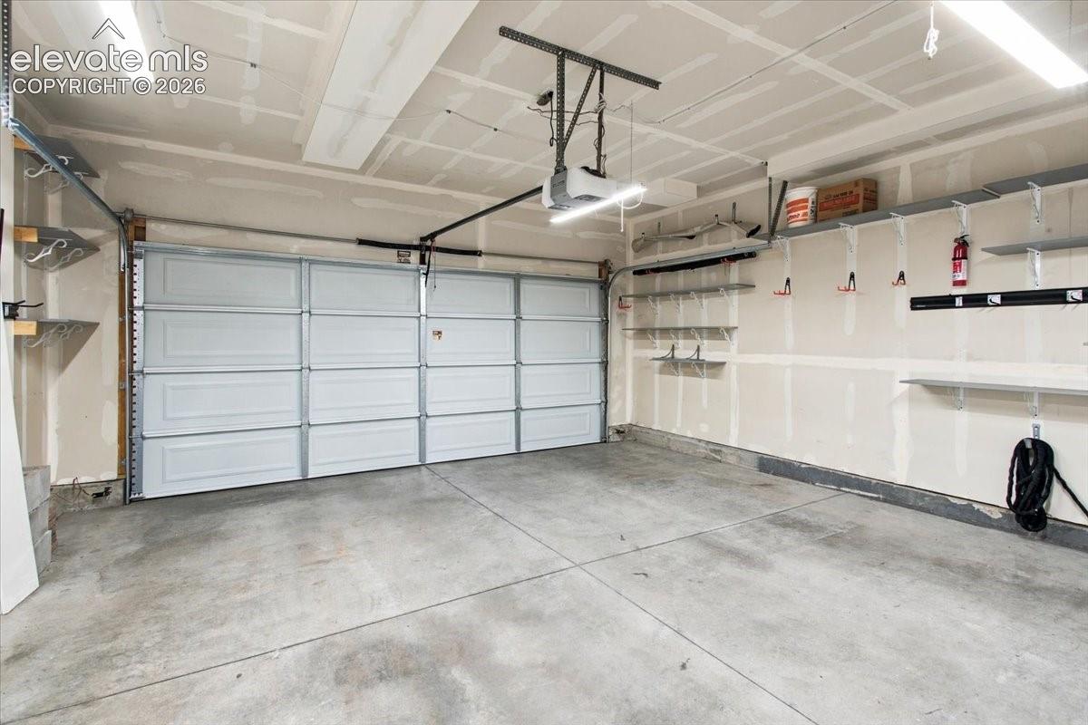 Attached garage featuring a concrete floor, built-in shelving, and overhead lighting