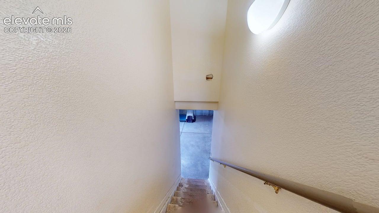 Stairwell featuring a textured wall finish, a handrail, and an overhead flush-mount light fixture