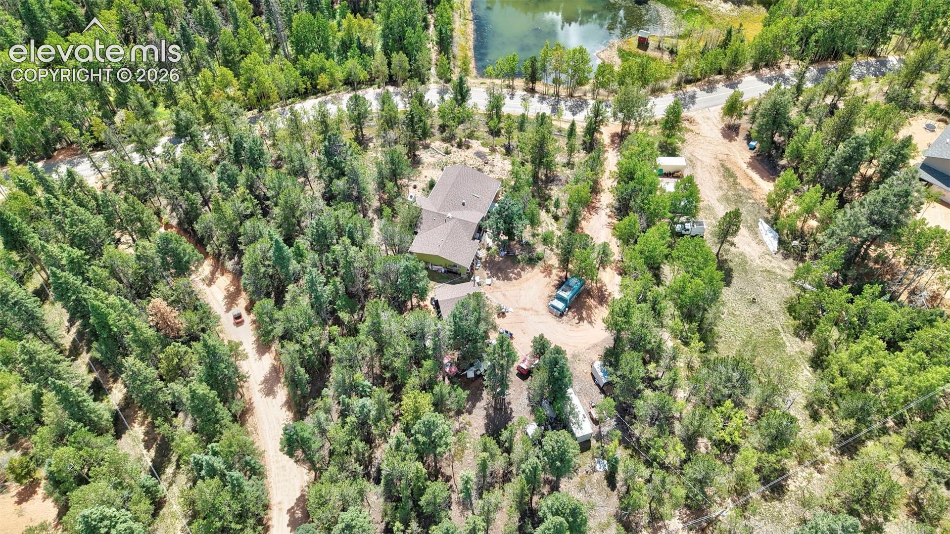 Wooded property with a private drive and a main residence featuring a brown roof
