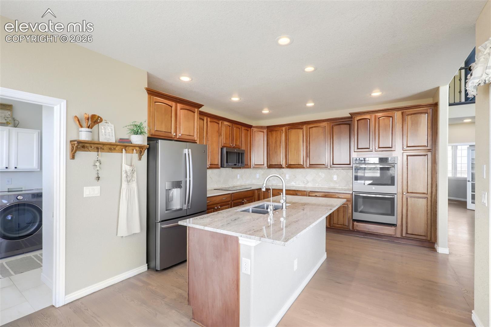 Step into a beautifully appointed kitchen featuring warm maple cabinetry, gleaming stainless-steel appliances, including double wall ovens, refrigerator, and microwave, along with an induction cooktop. Granite countertops and a spacious center island with a built-in sink provide both style and functionality, while the tile backsplash adds an elegant finishing touch. Hardwood flooring, recessed lighting.
