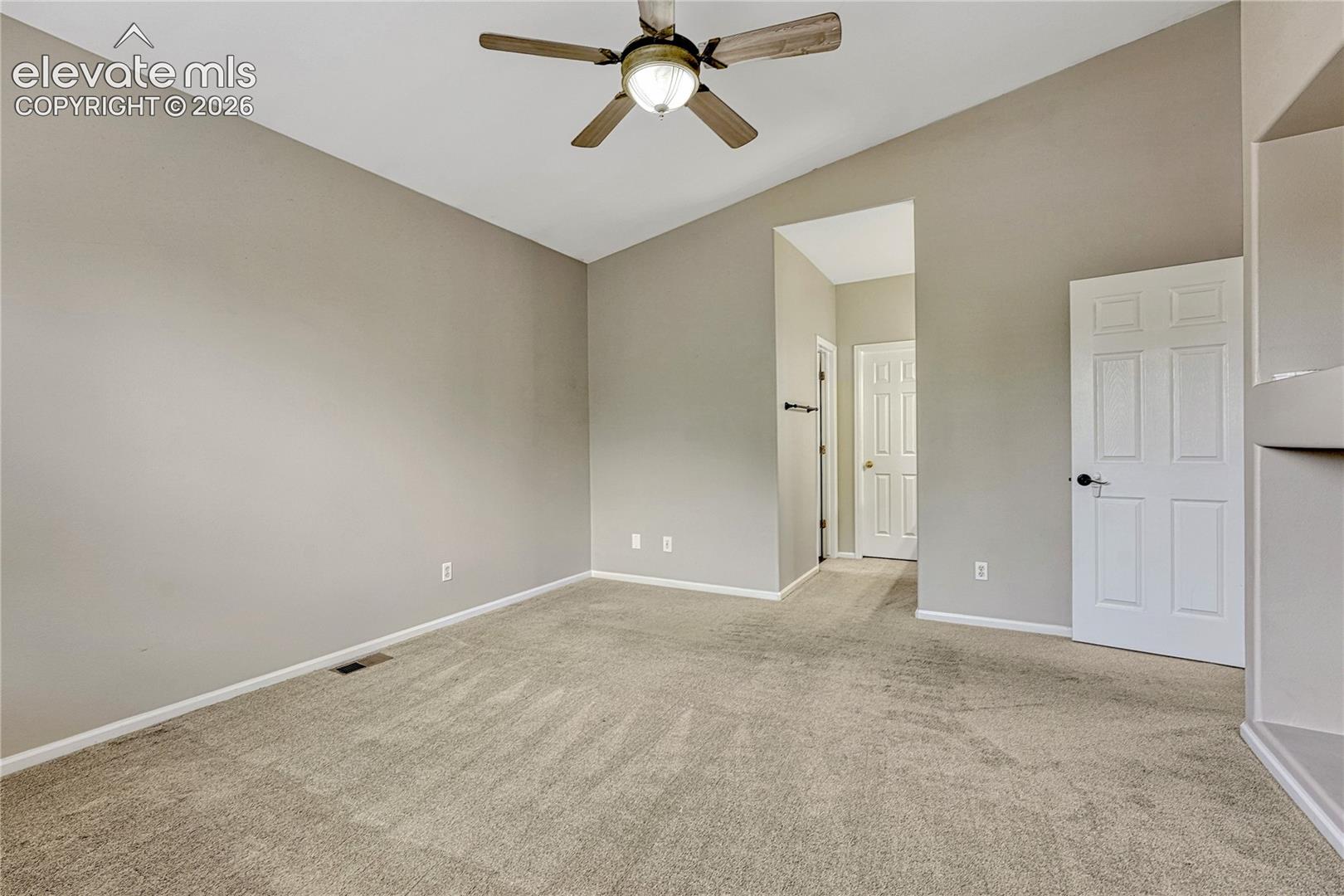 Vaulted ceilings featuring a central ceiling fan with integrated lighting, neutral wall tones, wall-to-wall carpeting, and a built-in recessed shelving niche