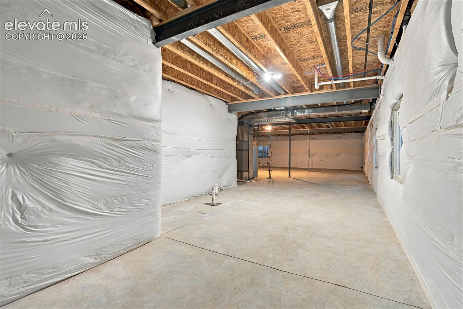 Unfinished lower level featuring concrete flooring, structural steel beams, exposed ceiling joists, and insulated wall wrap