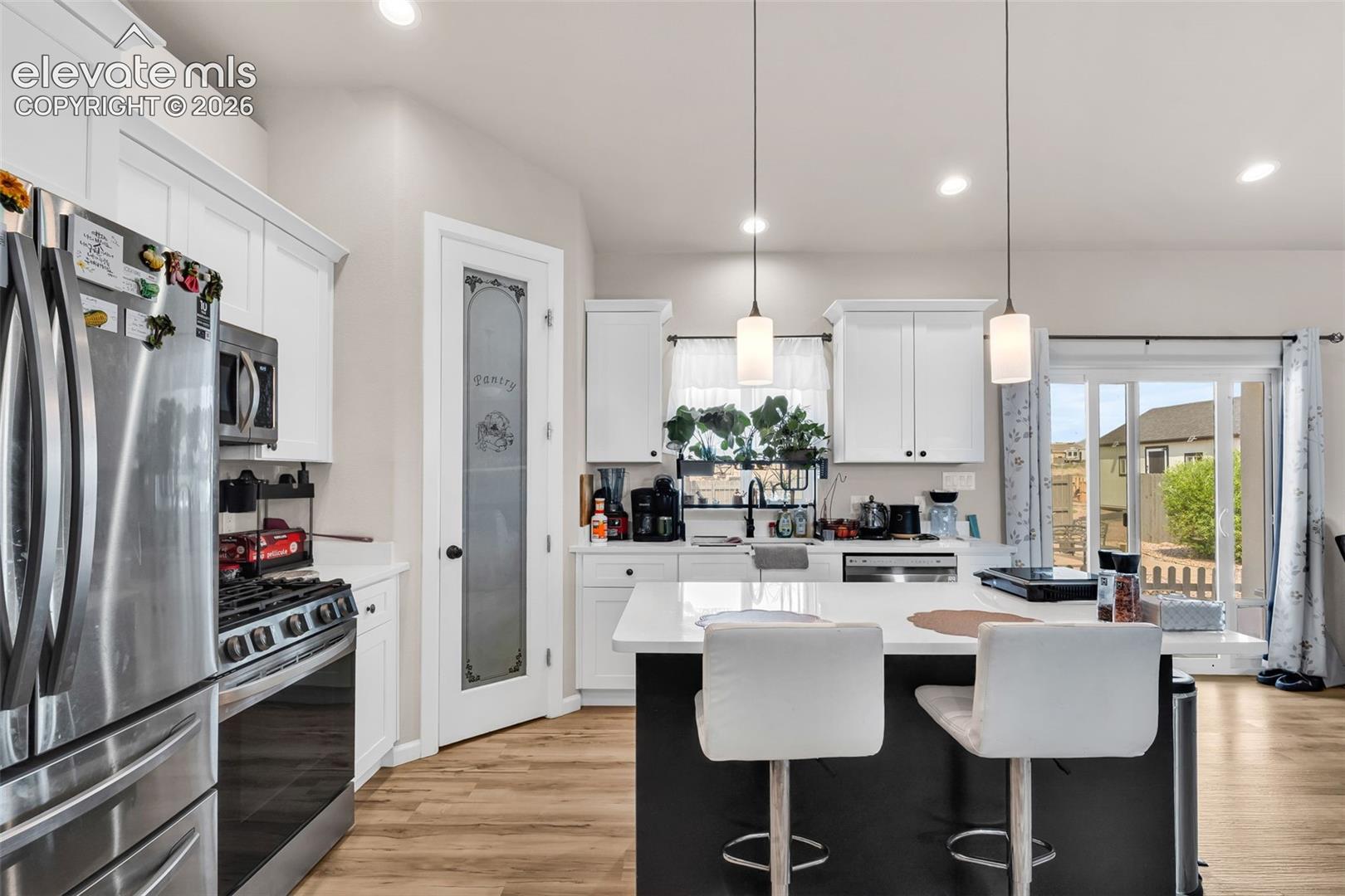 Modern kitchen featuring white cabinetry, stainless steel appliances, a center island with pendant lighting, and wood-finish flooring