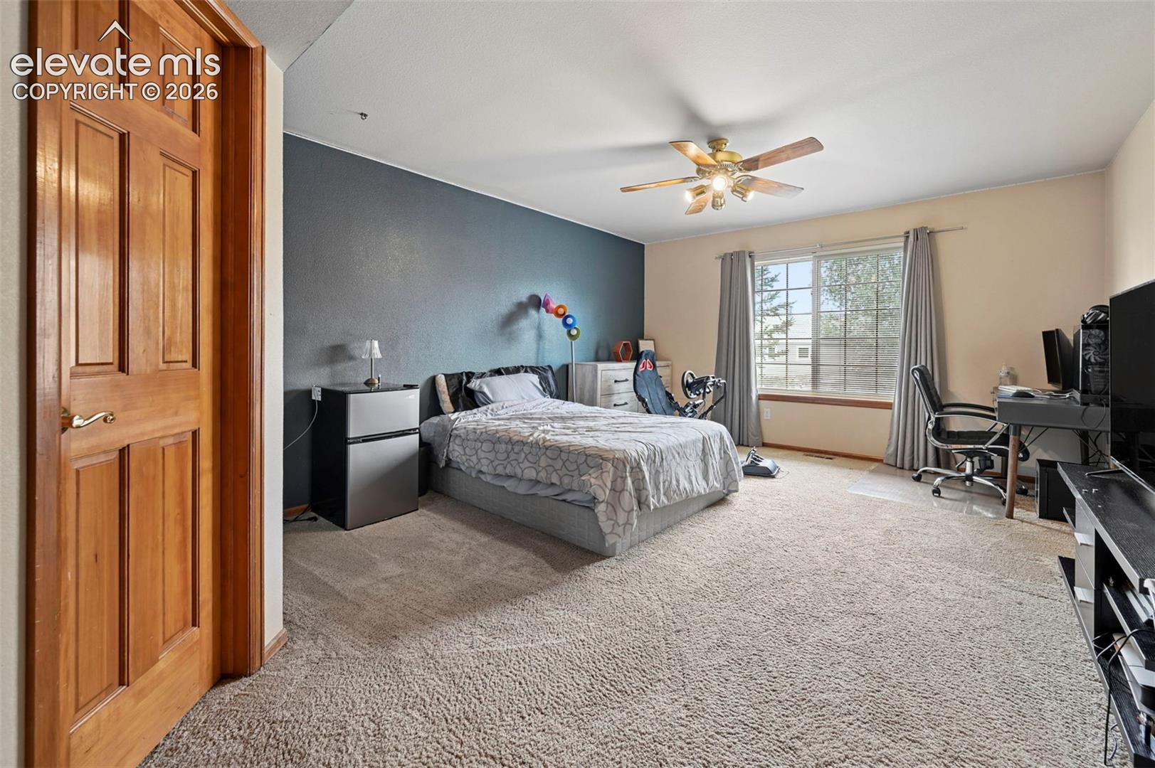 Main level bedroom with light-colored wall-to-wall carpeting, wood-paneled door, and a multi-pane window