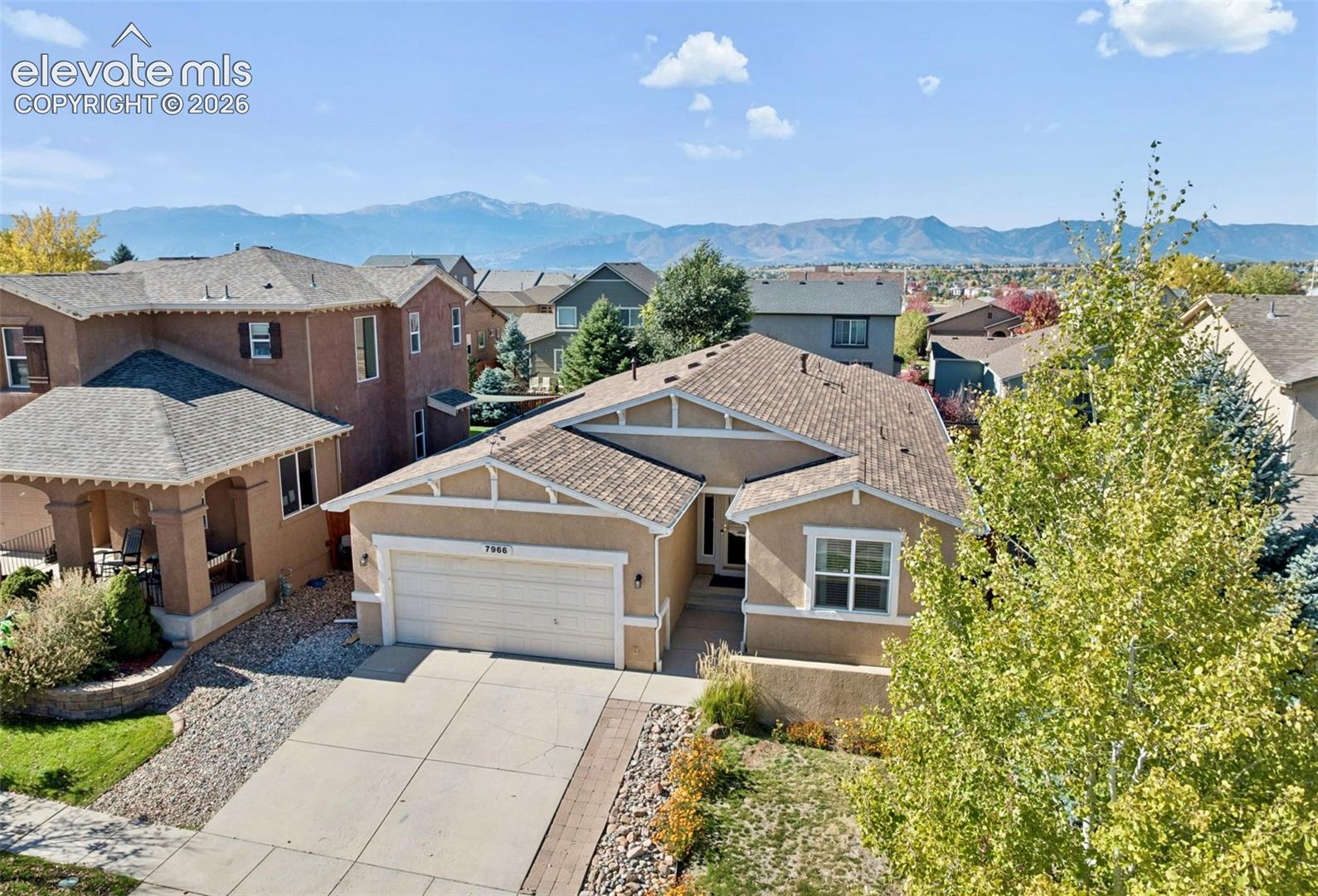 Stucco exterior with decorative gable detailing, asphalt shingle roofing, attached two-car garage, concrete driveway, and mountain backdrop