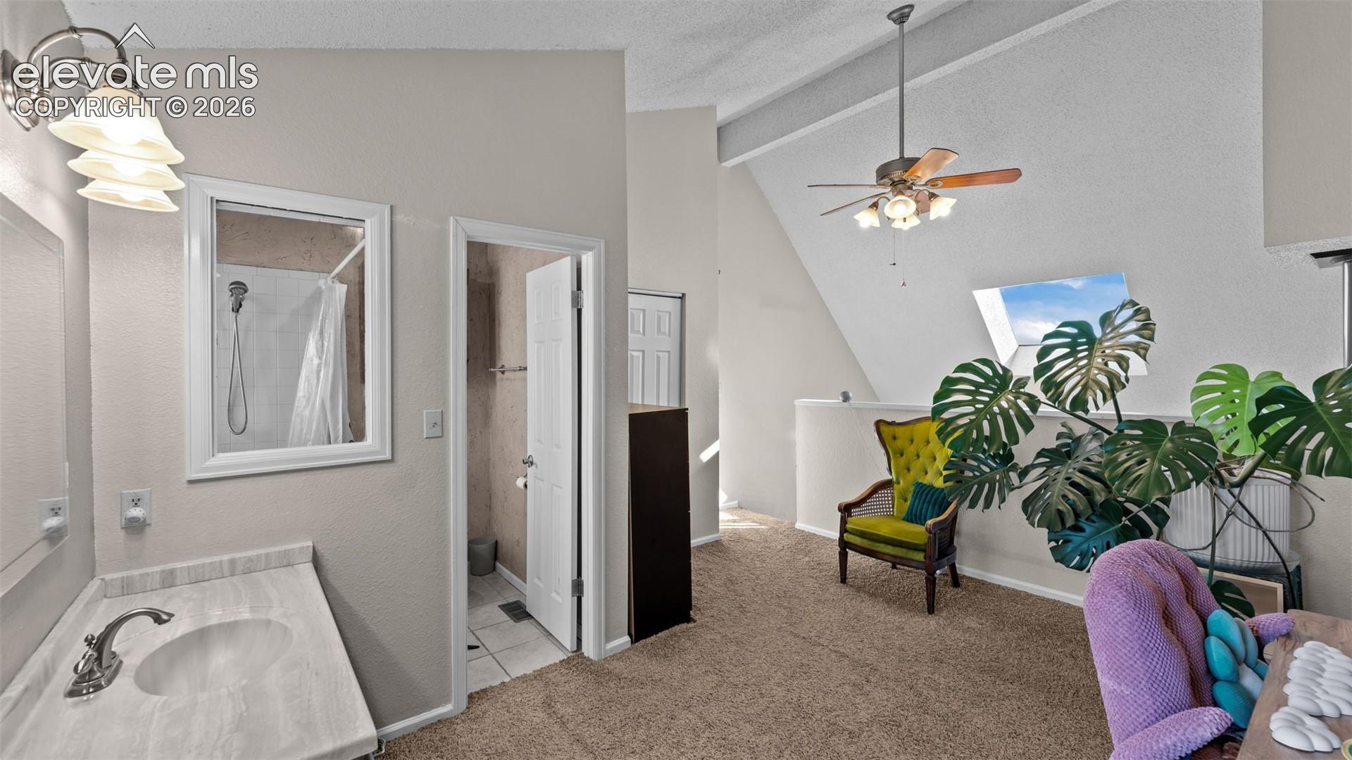 Vaulted ceiling featuring a skylight, ceiling fan with integrated lighting, wall-mounted vanity with a stone-finish countertop, and wall-mounted light fixtures