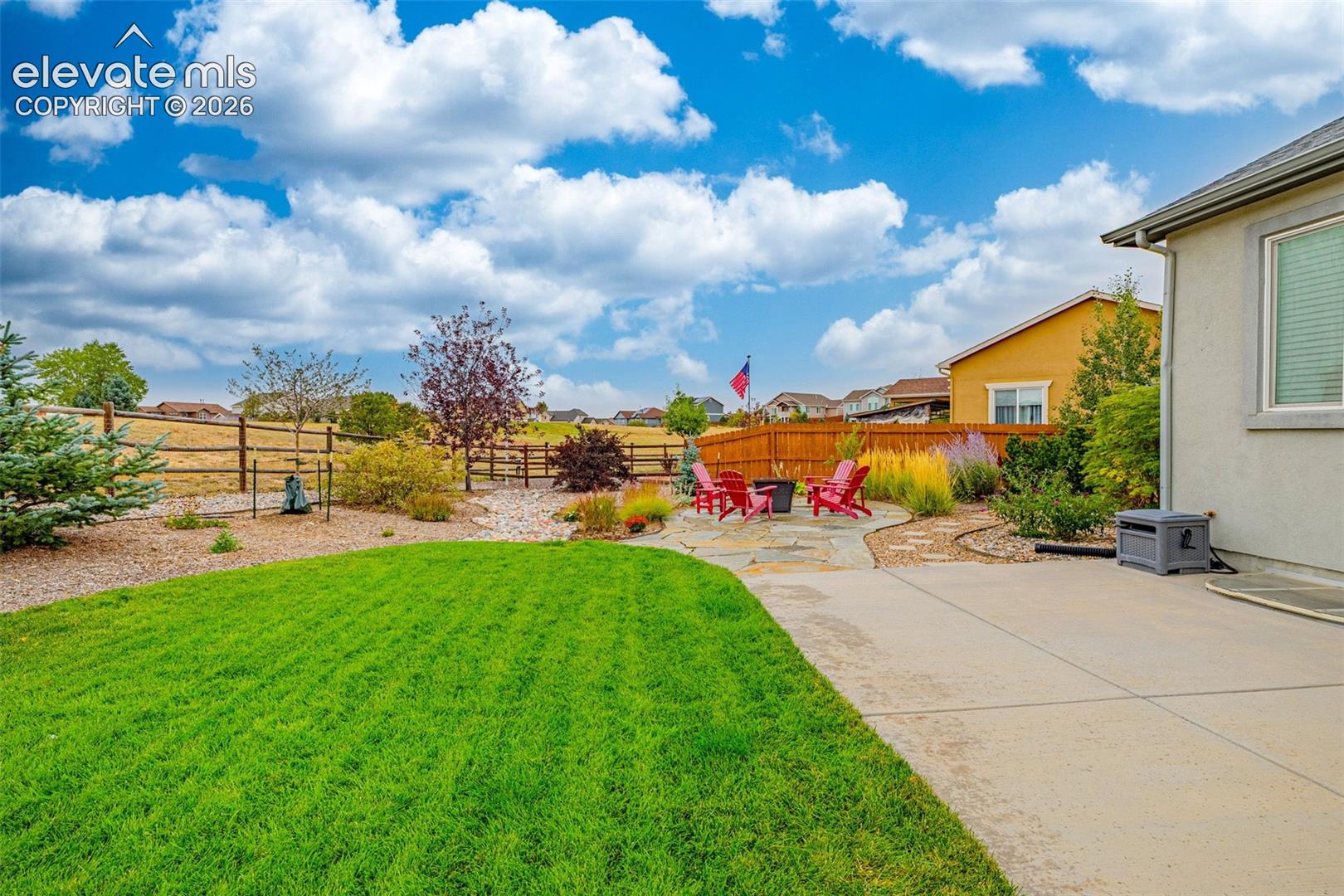 Rear yard featuring a concrete patio, irregular stone hardscaping, manicured lawn, and perimeter wood fencing