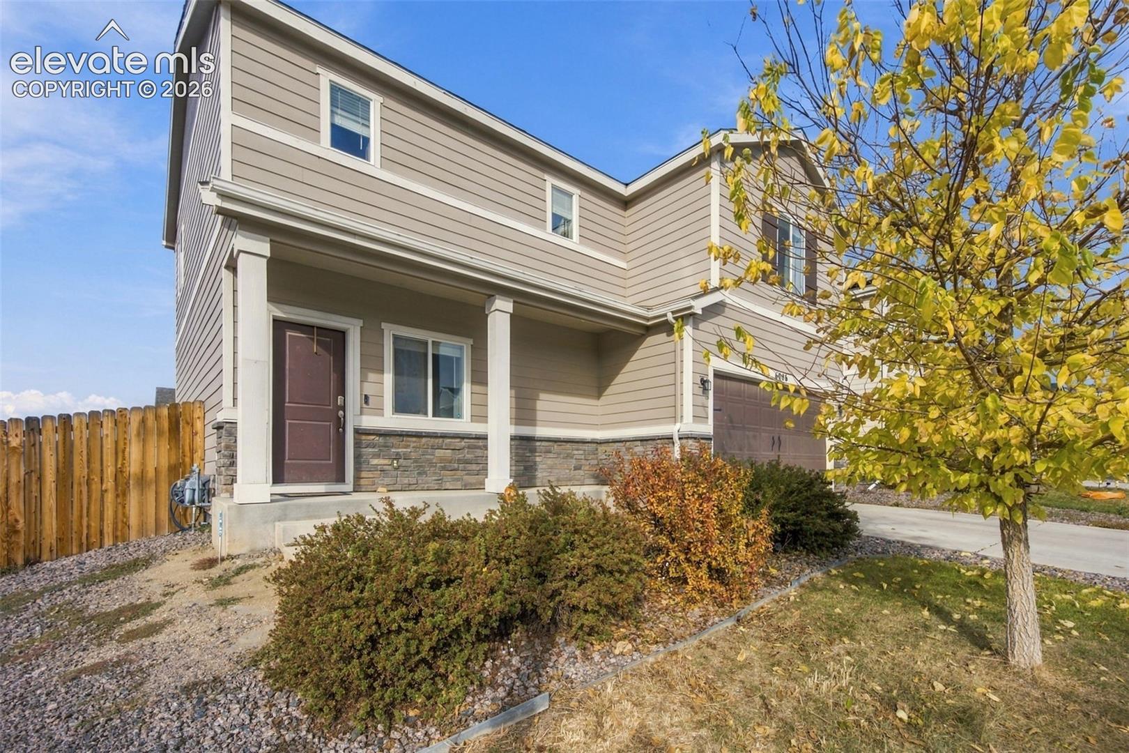 Two-story exterior featuring horizontal siding, a stone veneer foundation, a covered front porch with support columns, and an attached two-car garage