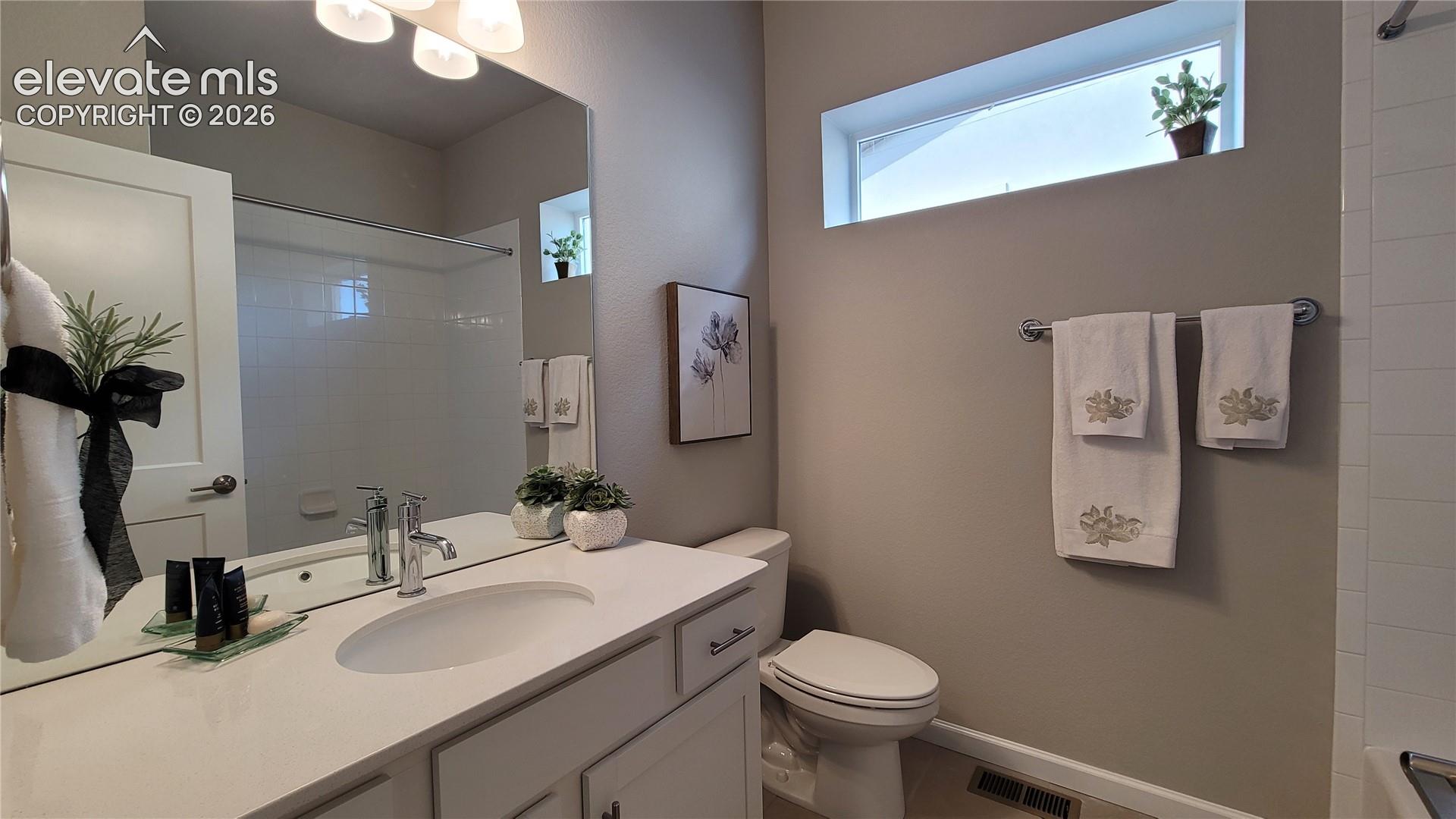 Bathroom featuring a white vanity with a quartz countertop, an oval under-mount sink, chrome faucet, plated mirror, and a window