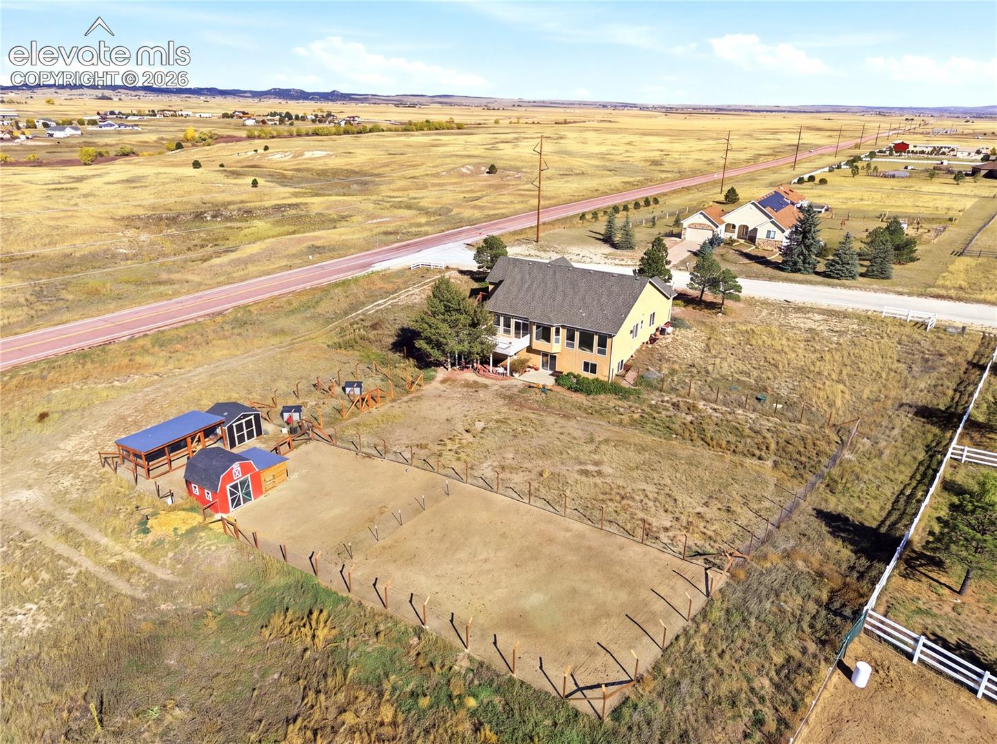 Aerial view of a multi-level residence featuring an attached garage, a detached barn structure, a fenced perimeter, and an expansive open-lot landscape