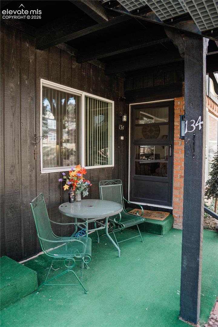 Front porch featuring a textured green floor, dark wood-paneled exterior, and white-framed windows