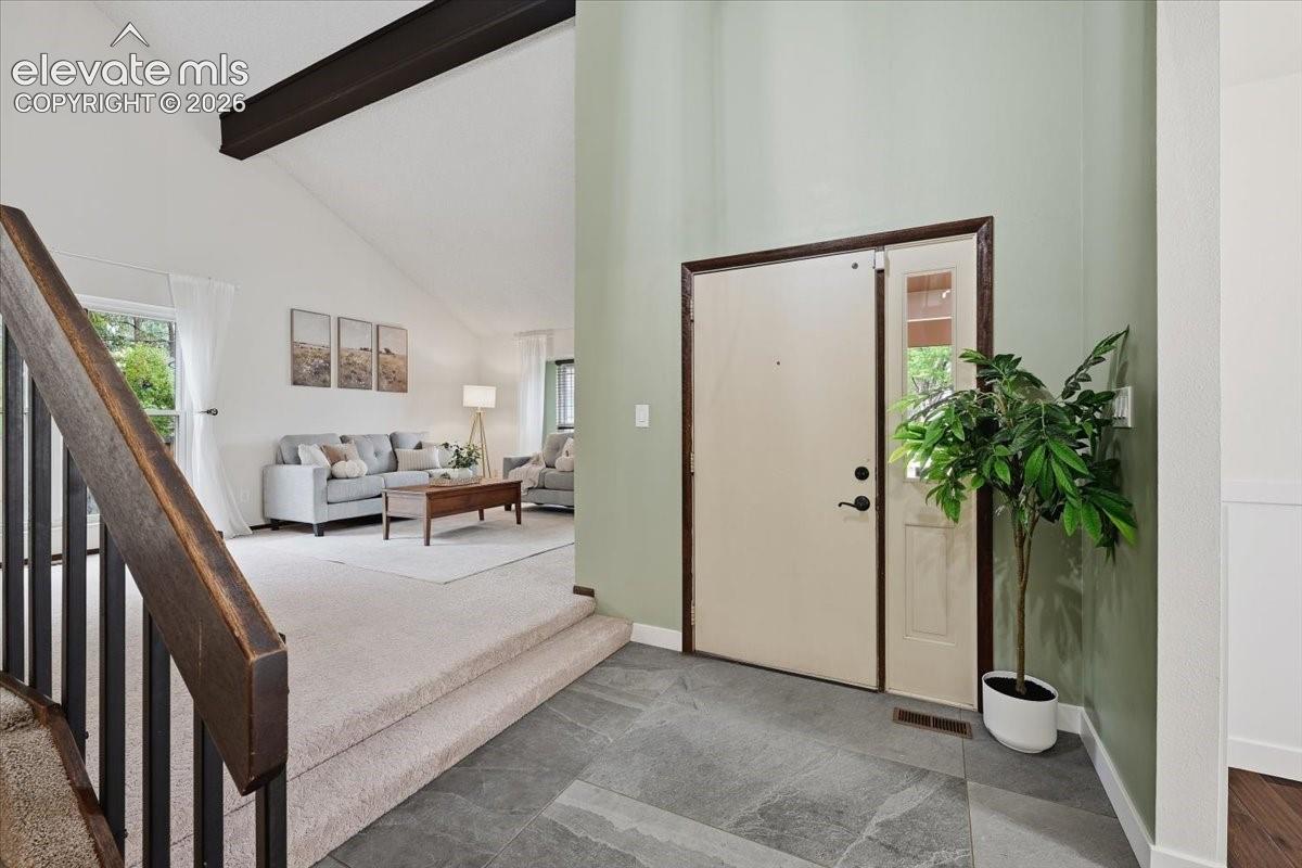 Tiled entryway leading to a living area with vaulted ceilings and exposed beams