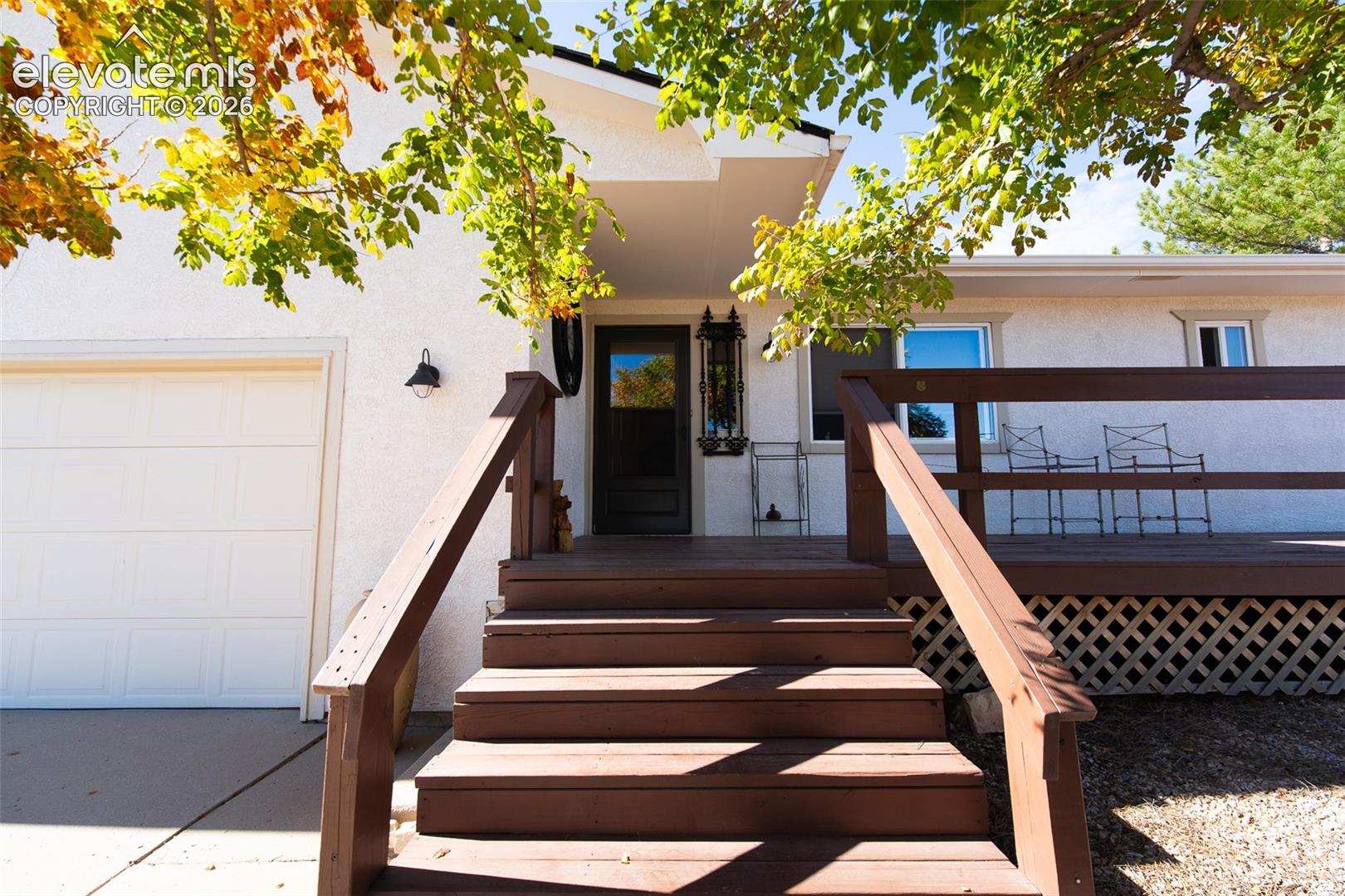 Stucco exterior with wood-tone deck, stairs, railing, and attached garage