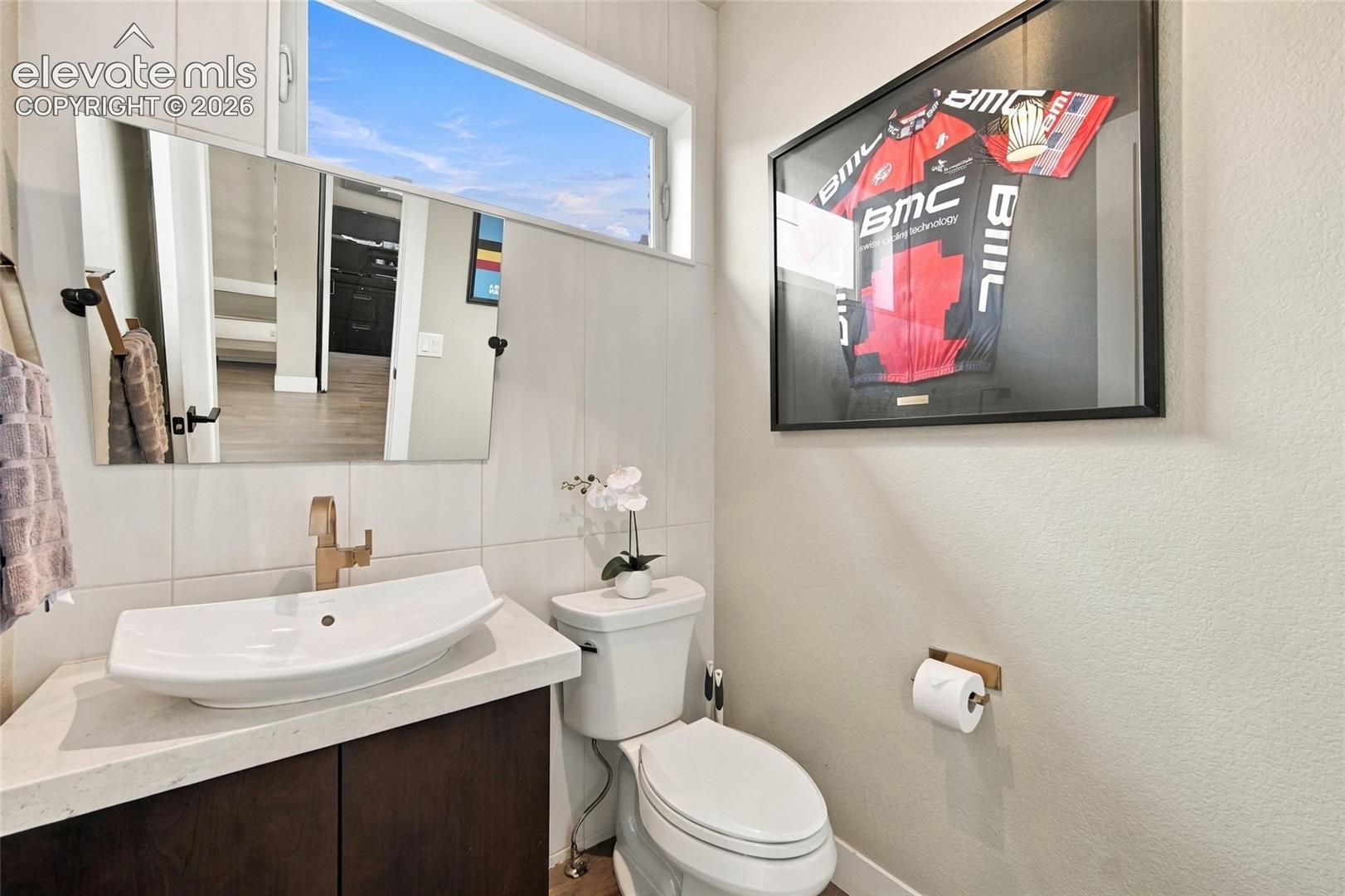 Floating vanity featuring a stone-composite countertop, rectangular vessel sink, metallic faucet, rectangular wall-mounted mirror, and horizontal transom window