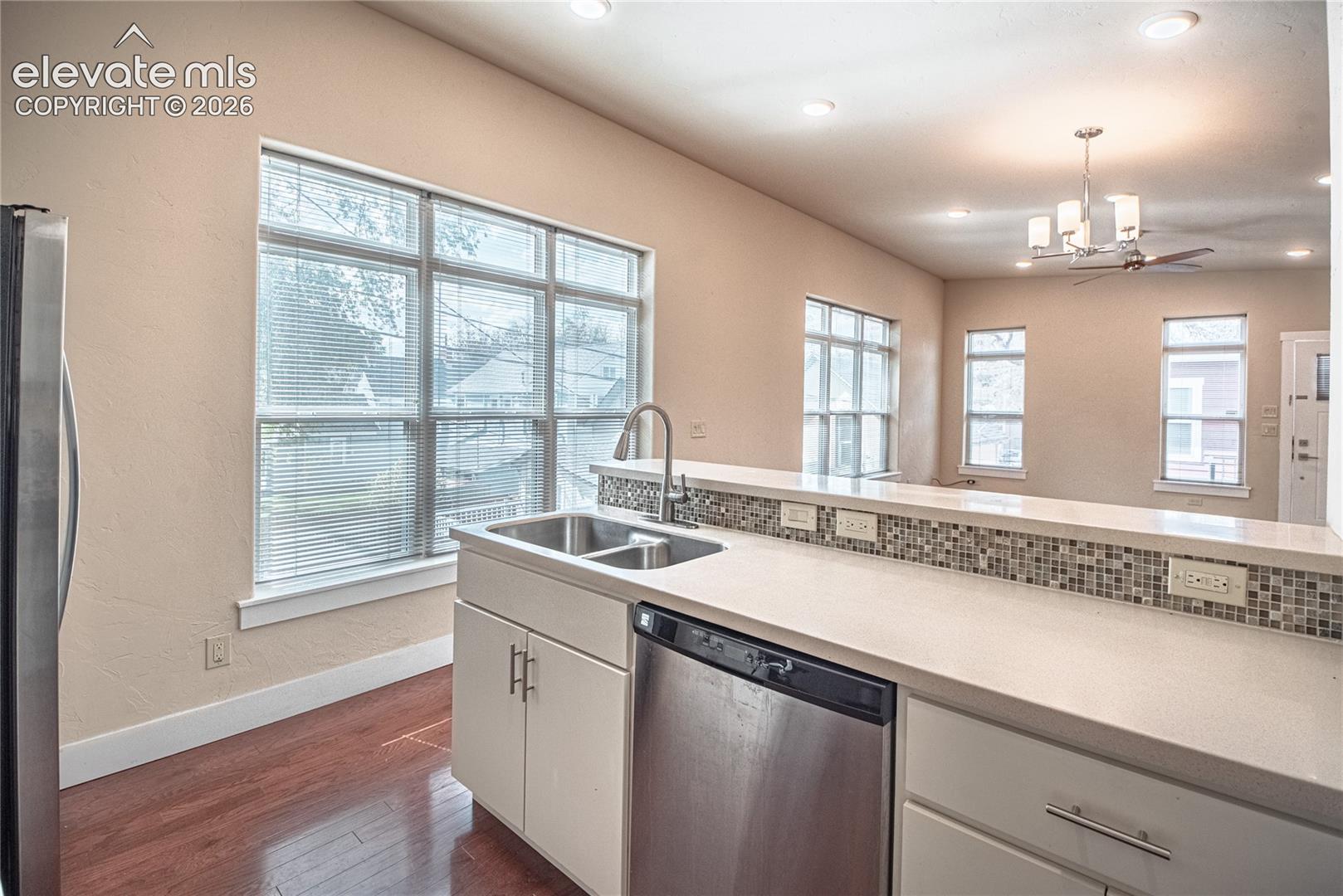 Kitchen featuring a stainless steel double sink, a built-in dishwasher, light-toned countertops, and a mosaic tile backsplash