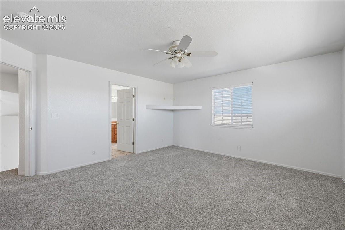 Spacious room featuring light gray carpet flooring, a ceiling fan with integrated lighting, and a window with horizontal blinds