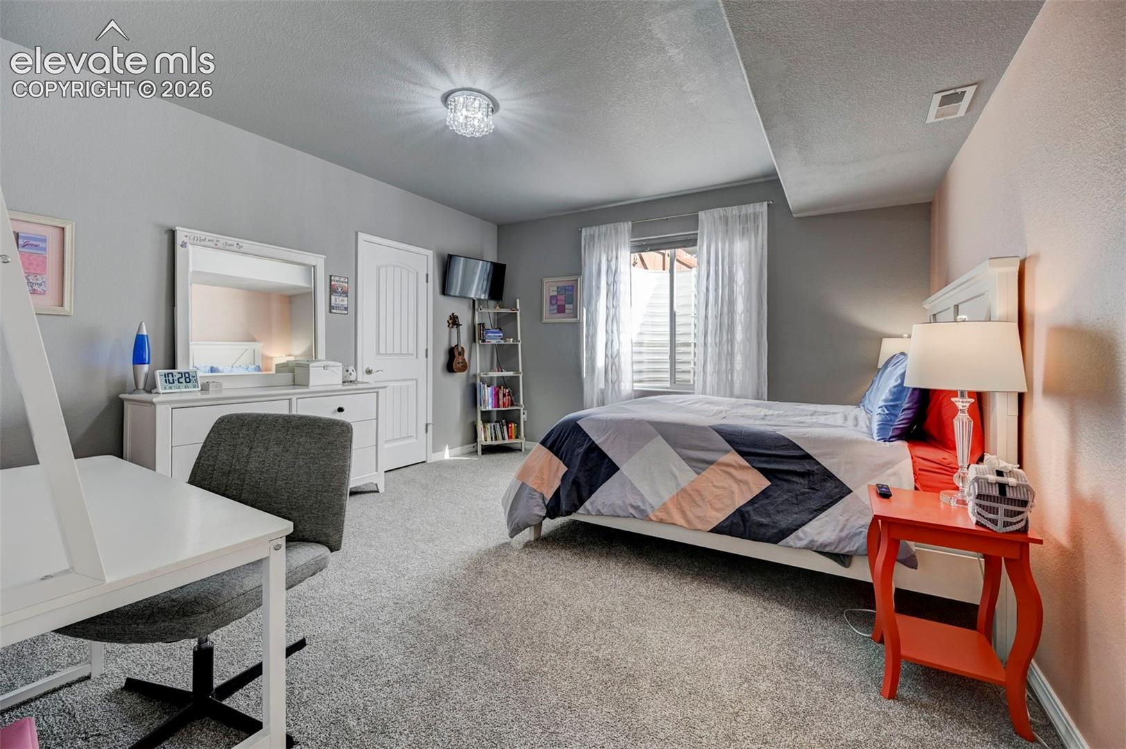 Carpeted room featuring a window with blinds and white sheer curtains, a white paneled door, and a crystal flush mount ceiling light