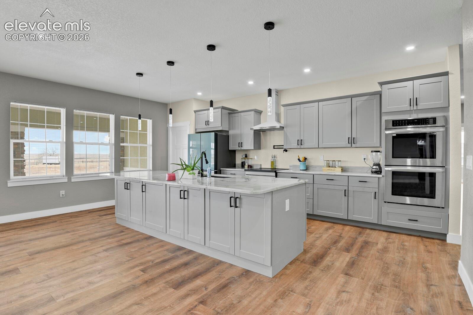 Kitchen featuring gray shaker-style cabinetry, a large center island with a white countertop, wood-finish flooring, recessed lighting, and stainless steel appliances including a wall oven and microwave