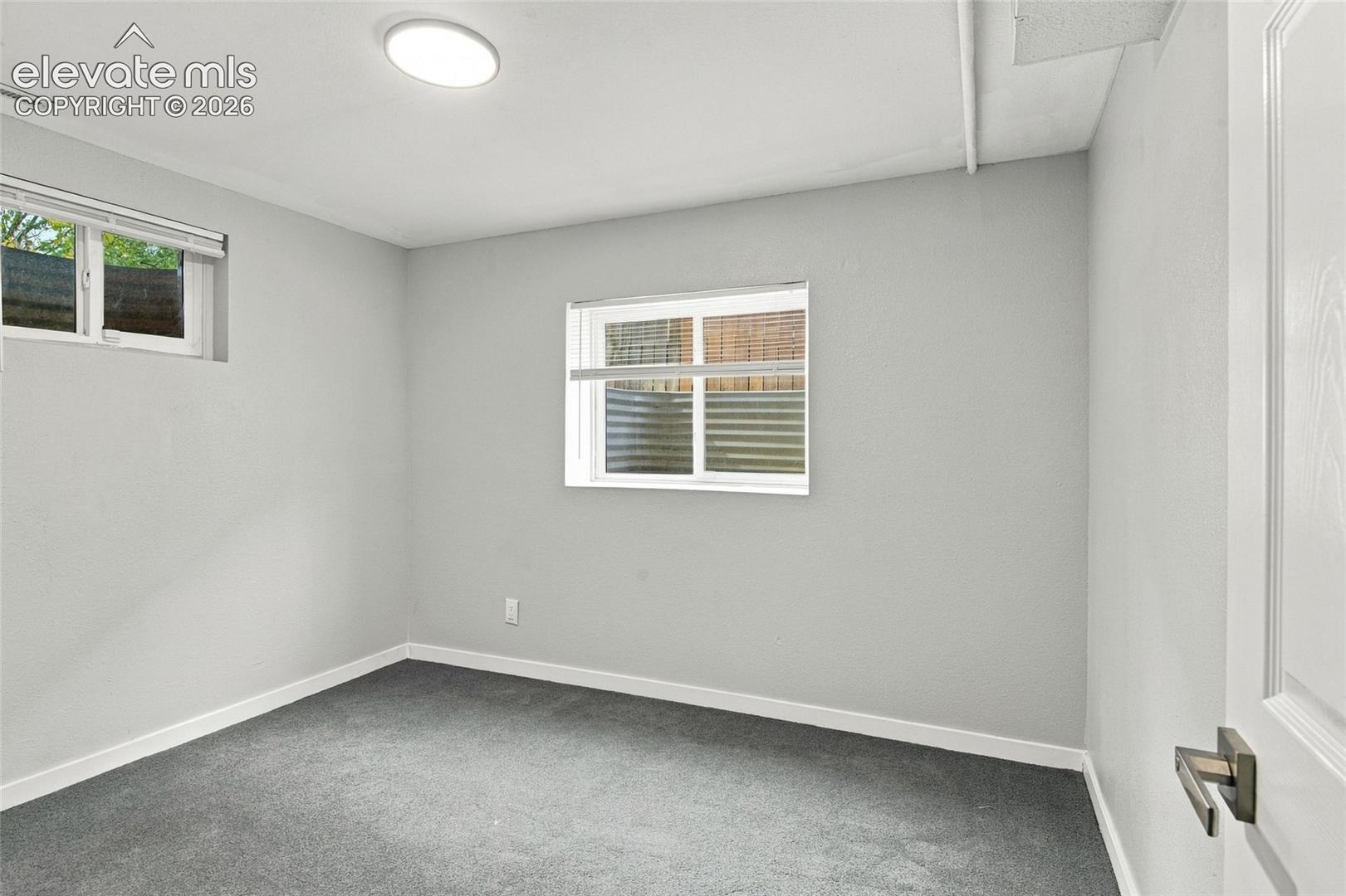 Neutral-toned room featuring grey wall-to-wall carpeting, two sliding windows, and a flush-mount overhead light fixture