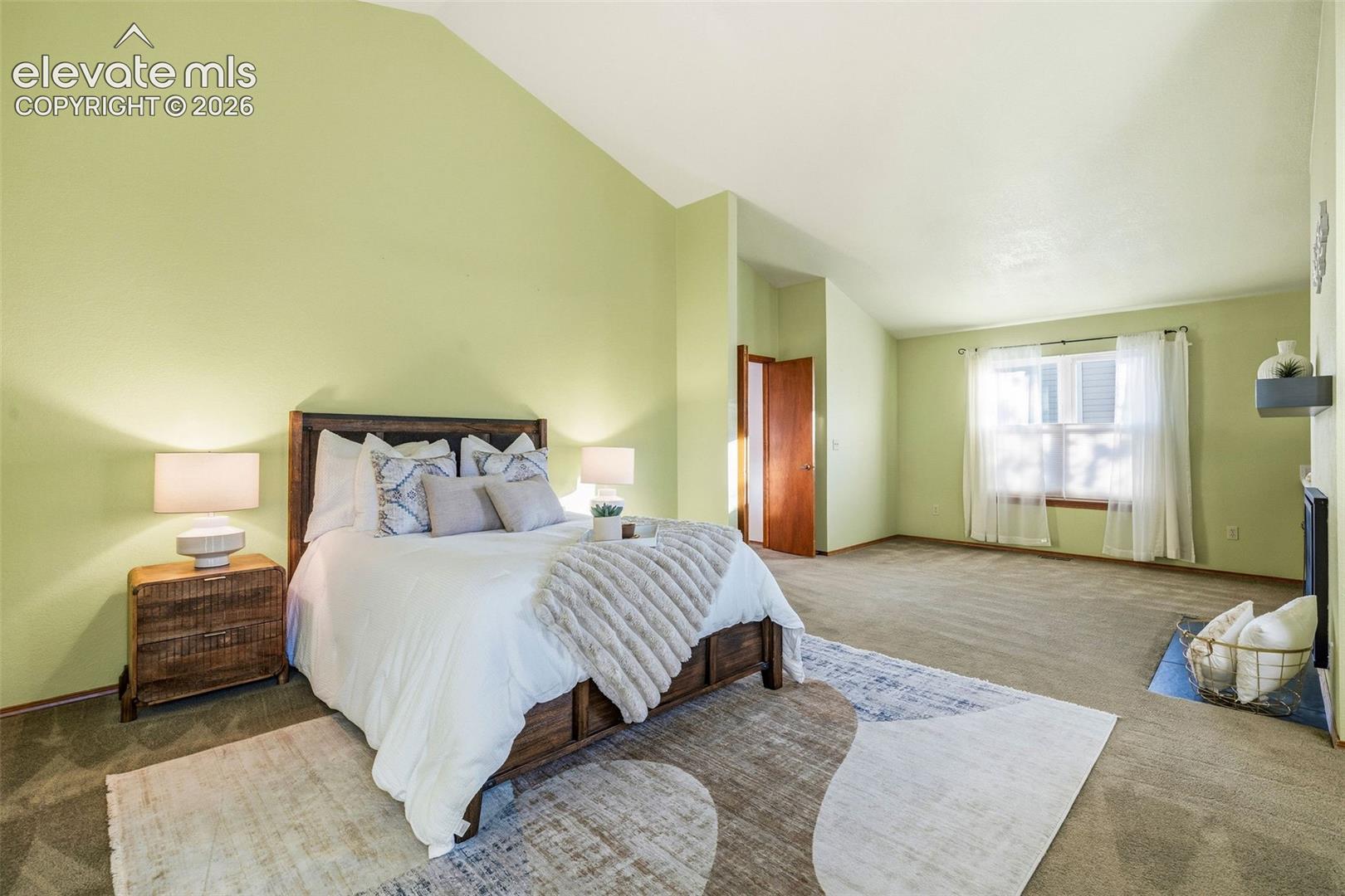Vaulted ceilings, carpeted flooring, large window with natural light, and a fireplace with a black surround