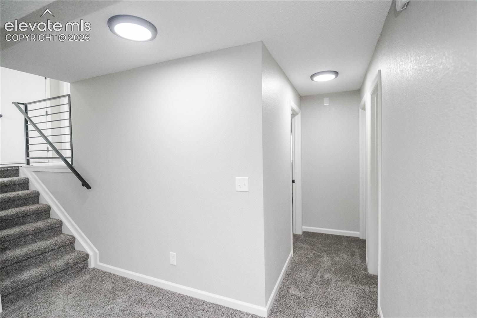 Staircase featuring gray wall-to-wall carpeting, industrial-style metal horizontal railing, and integrated flush-mount ceiling lighting