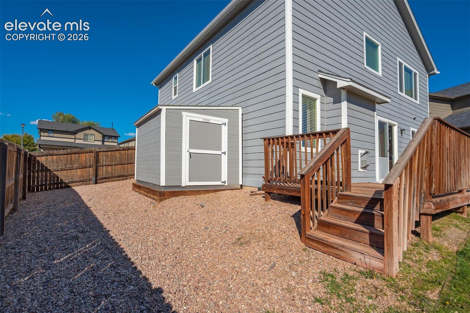 Rear exterior featuring a wooden deck with stairs, sliding glass door, an exterior Tuff shed, and a privacy fence