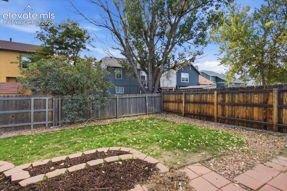 Private backyard featuring a wood privacy fence, lawn area, stone-paved patio, and stone-bordered garden bed