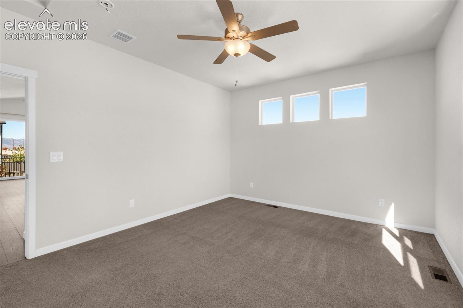 Neutral-toned interior space featuring three high-placement windows, carpeting, and a central ceiling fan with an integrated light fixture