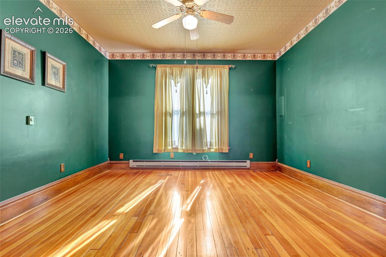 Room featuring wood-finish flooring, textured ceiling, central ceiling fan, and decorative wallpaper border