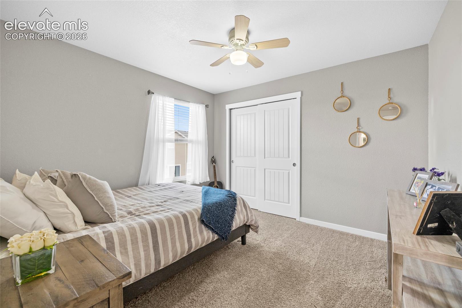 Neutral-toned room featuring plush wall-to-wall carpeting, dual-panel sliding closet doors, and a ceiling fan with integrated light fixture