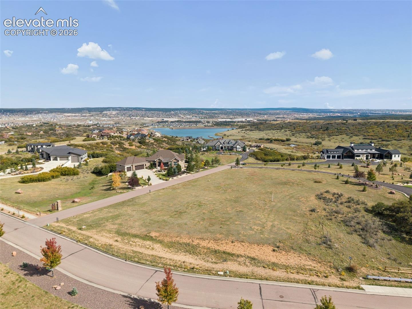 Expansive undeveloped residential lot featuring paved street access, native landscaping, and distant water and mountain terrain