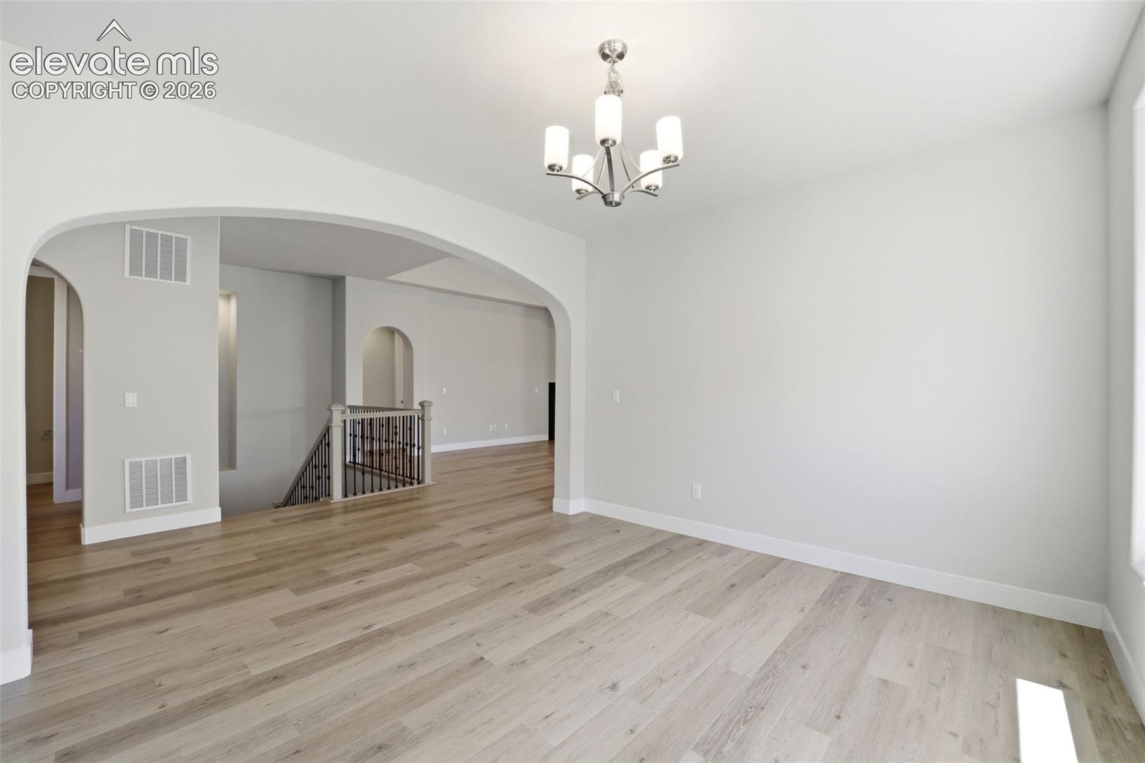 Neutral interior featuring wood-finish flooring, multi-arched architectural openings, a five-light metallic chandelier, and a decorative staircase railing