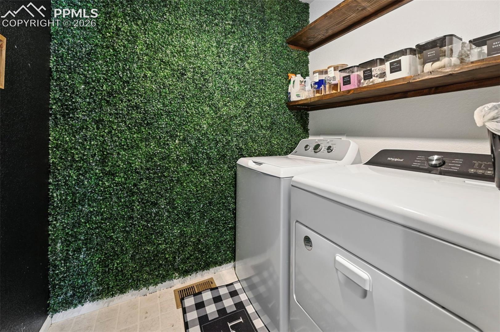 Laundry space featuring a unique green wall texture, white appliances, and a wood-finish floating shelf