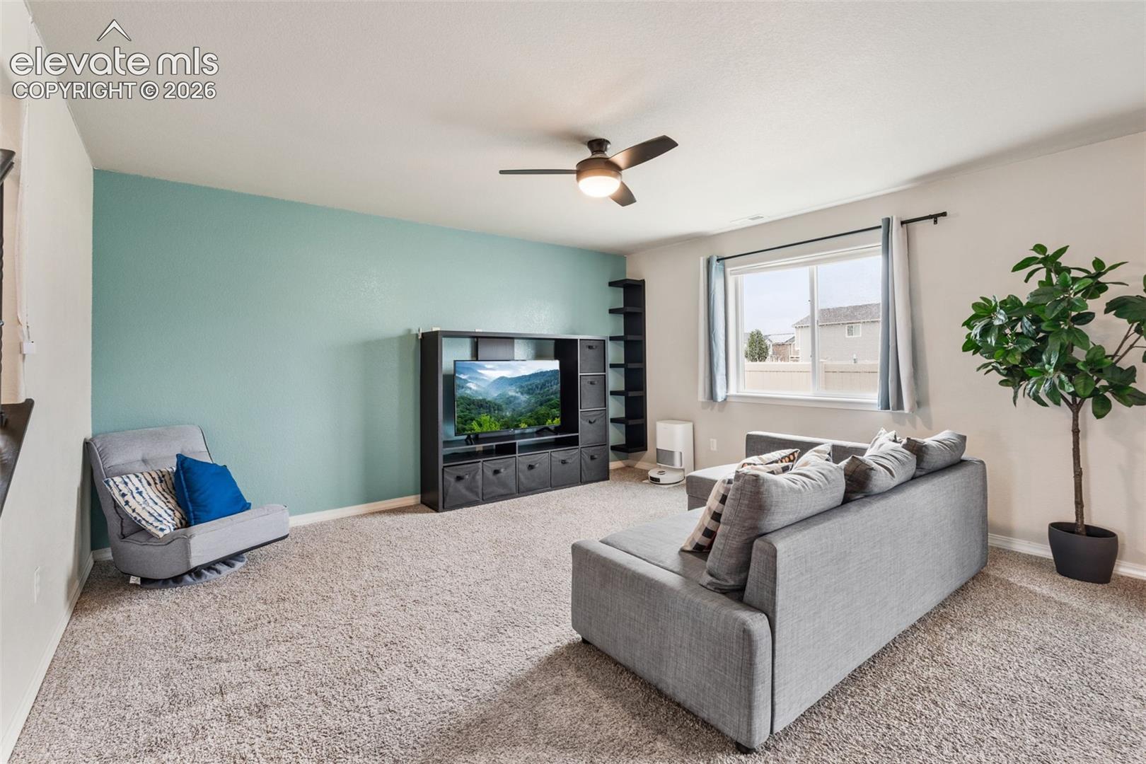 Carpeted living space featuring a window, built-in shelving, and a ceiling fan with integrated lighting