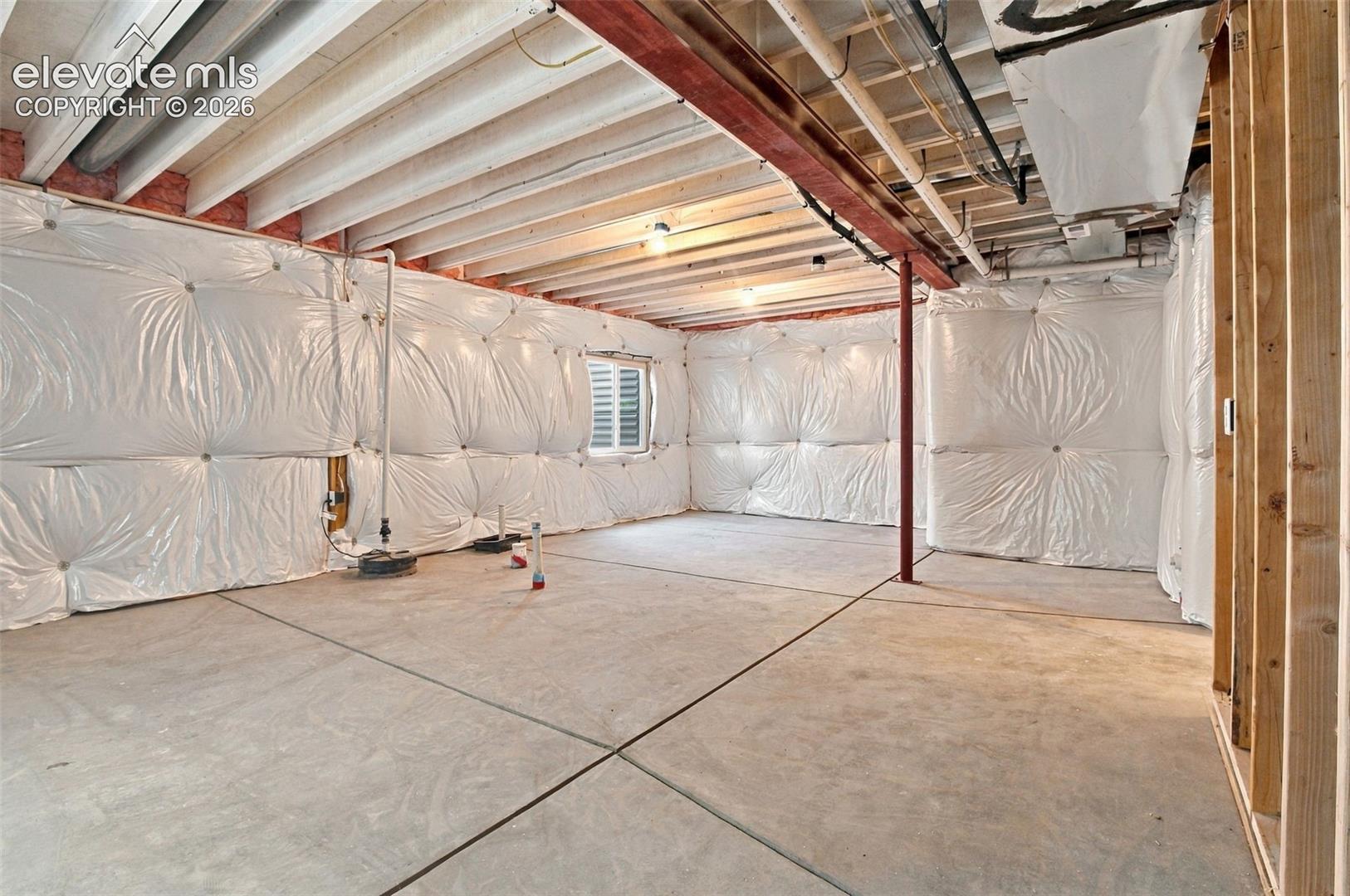 Unfinished lower level with concrete flooring, exposed ceiling joists, steel support beam, and insulated foundation walls