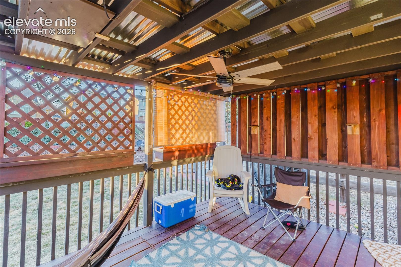 Covered deck with a corrugated metal ceiling, wood-finish flooring, and a ceiling fan