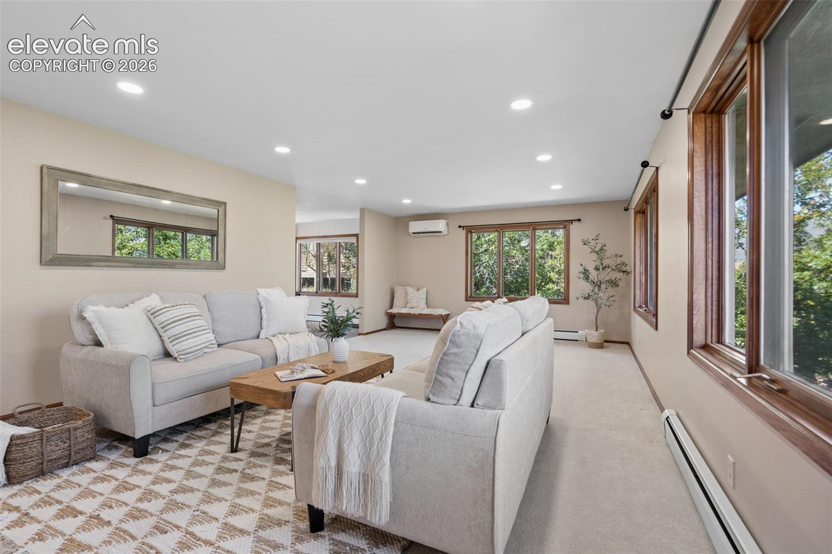 Recessed ceiling lighting, numerous windows with wood-finish frames, light-toned wall paint, and wall-mounted climate control unit