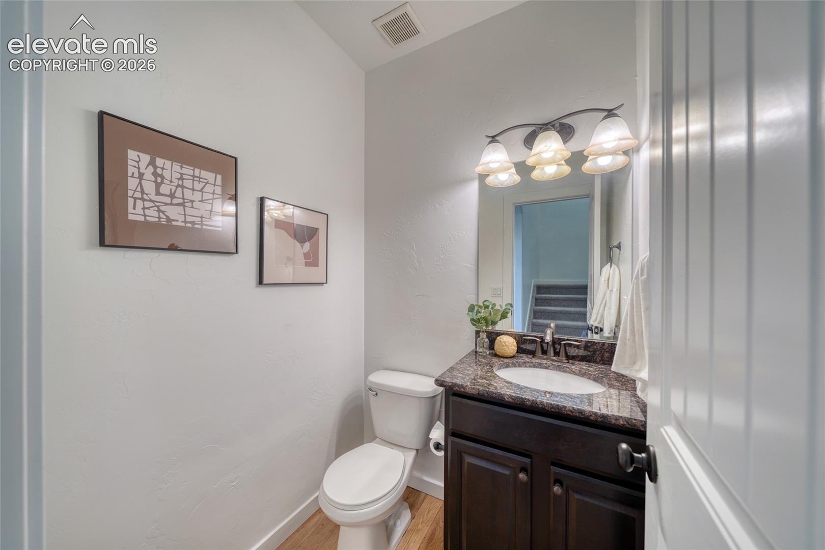 Powder room featuring a dark wood-finish vanity, stone-look countertop, integrated sink, and an overhead vanity light fixture