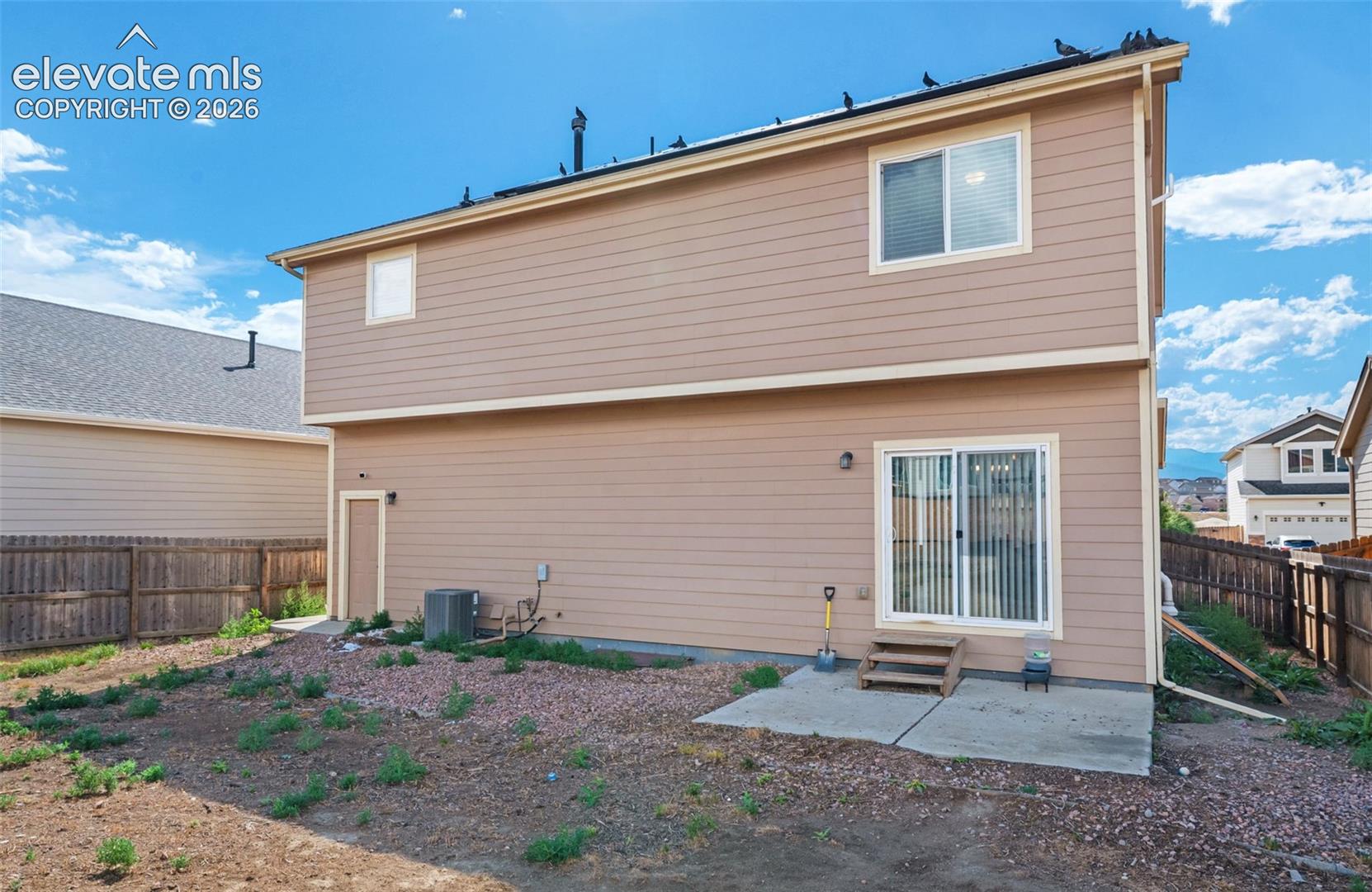Two-story residence featuring horizontal lap siding, a rear concrete patio, sliding glass door, and wooden fencing