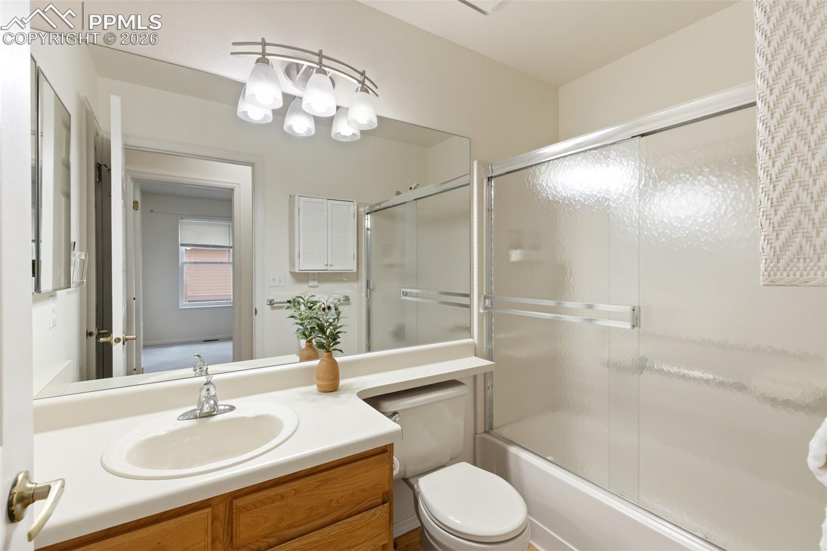 The bathroom features a vanity with a white countertop and a built-in sink, a large wall-mounted mirror, and a shower-tub combination with a sliding glass door