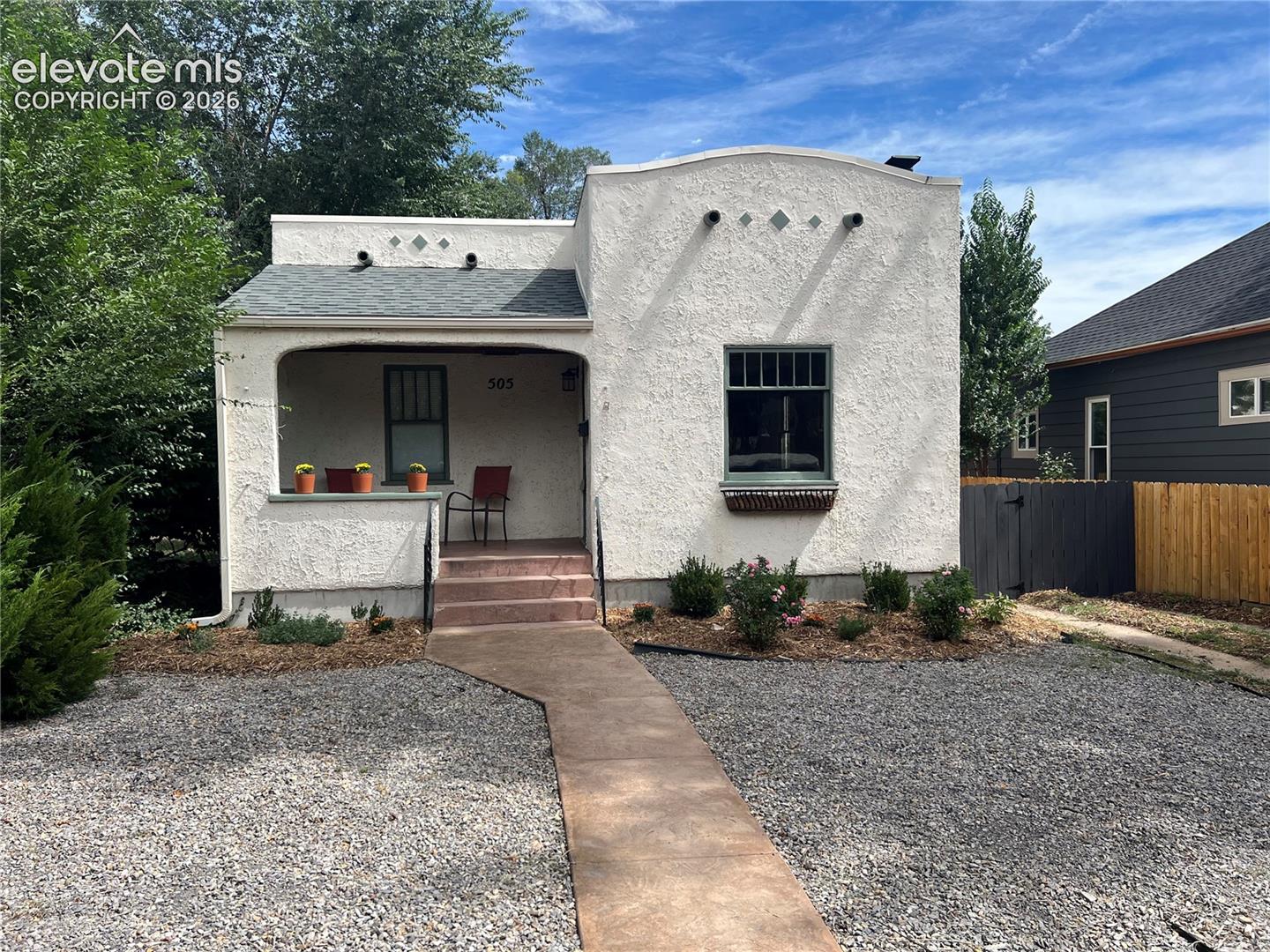 Main House - Stucco exterior with a covered porch, established landscaping, and a xeriscaped front yard
