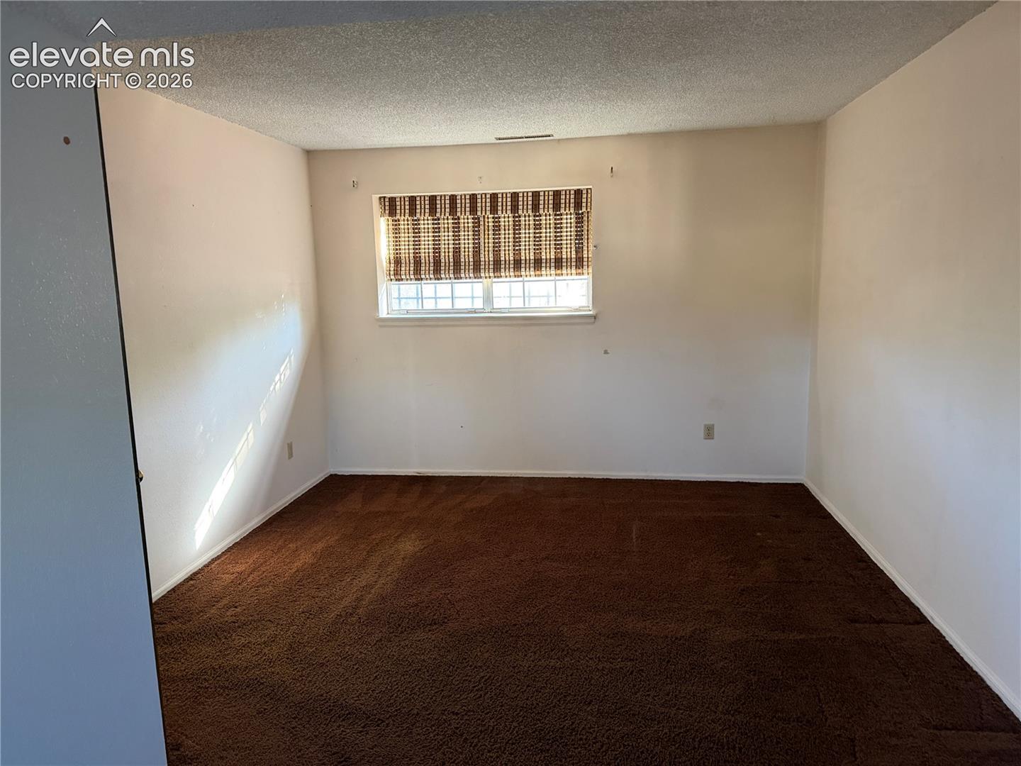 Bedroom 3 in lower level with interior featuring neutral walls, brown wall-to-wall carpeting, and a multi-pane window with a woven shade