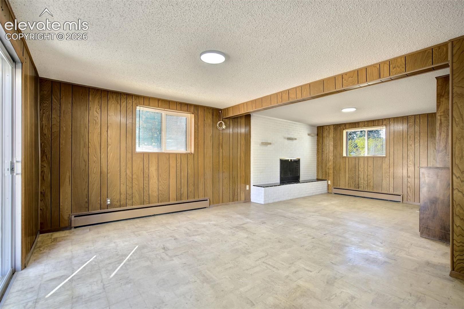 Interior space featuring wood-paneled walls, a white painted brick fireplace with a raised hearth, light-toned resilient tile flooring, and sliding glass exterior door