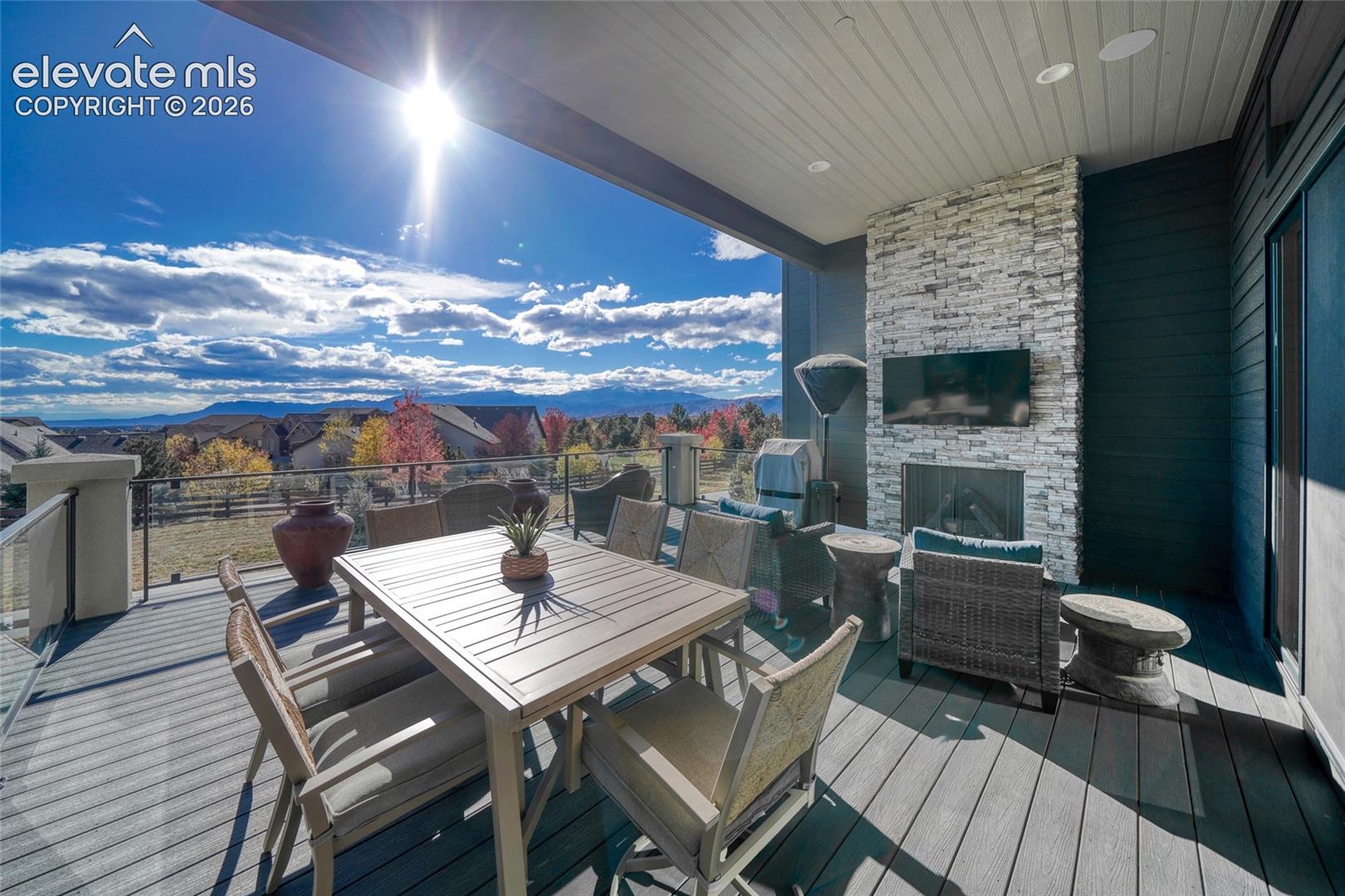 Covered deck featuring composite decking, stacked stone fireplace, recessed lighting, and metal railing