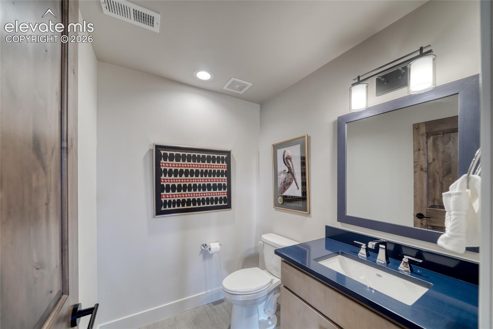 Bathroom featuring a vanity with a solid-surface countertop, rectangular undermount sink, framed wall mirror, polished chrome faucet, and recessed lighting