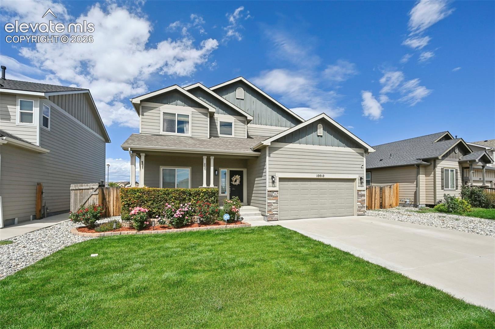 Two-story residence featuring composite siding, an attached garage, a covered front porch, and a landscaped front yard with a concrete driveway